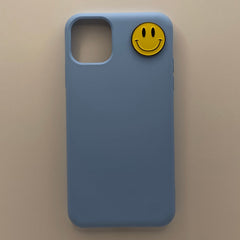 Pinkgul.no light blue phone case featuring a decorative yellow metal smiley face sticker attached to the back