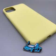 Pinkgul.no decorative metal sticker featuring a blue sports car with open doors, placed on a yellow phone case.
