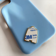 Pinkgul.no decorative metal sticker with 3M adhesive backing placed on a light blue phone case
