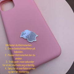 Pinkgul.no decorative silver metal sticker applied to a smooth pink phone case for custom decoration.