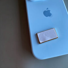 Pinkgul.no decorative rectangular metal sticker with a gold border attached to a light blue smartphone case