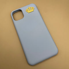 Pinkgul.no decorative gold metal crown sticker applied to a light blue smartphone case on a beige background