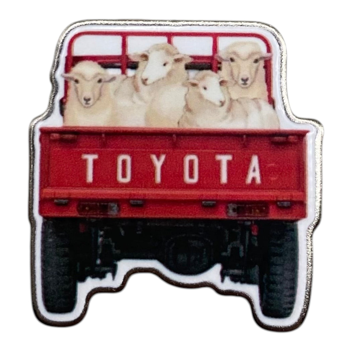 Pinkgul.no decorative metal sticker featuring a red Toyota pickup truck carrying sheep in the cargo bed